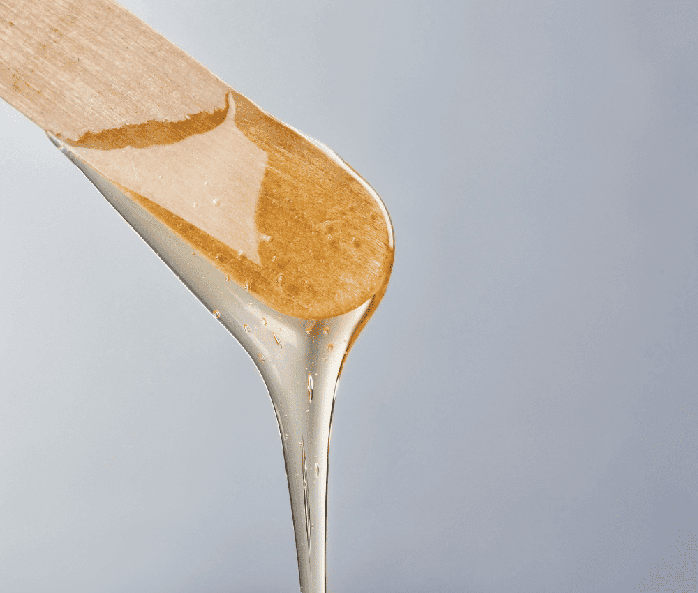 Honey dripping from a wooden dipper against a light background.