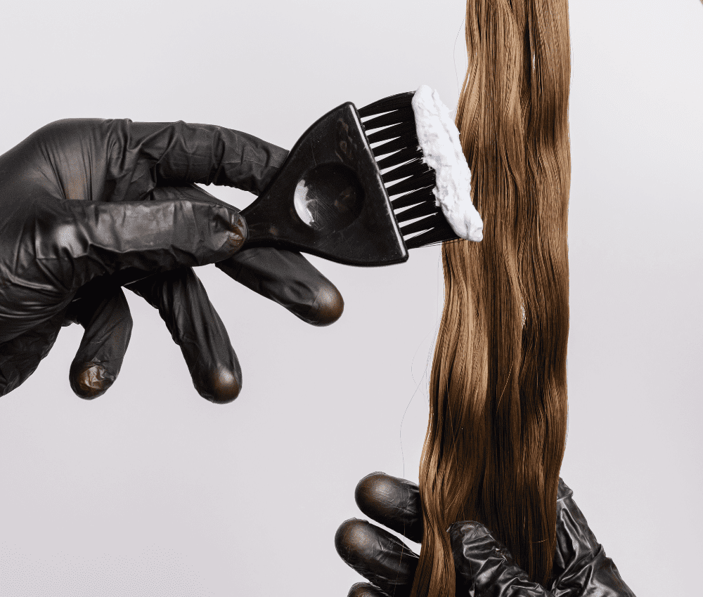 Gloved hands applying hair dye with a brush on long hair.